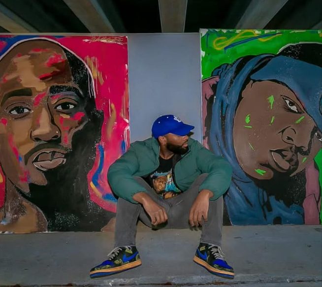 Willie Austin crouched under an overpass between his portraits of 2Pac and Biggie