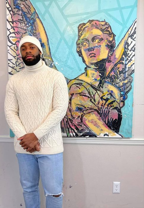 Willie Austin in a white sweater and beanie beside his painting of an angel on turquoise