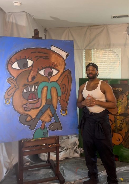 Willie Austin in his studio beside a large abstract face painted on a blue canvas