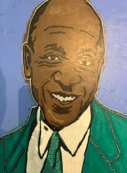 Portrait of Coach Willie Maxey smiling, in a green jacket and tie on a lavender background
