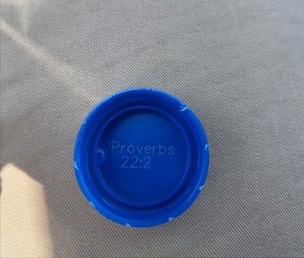 A blue bottle cap printed with Proverbs 22:2