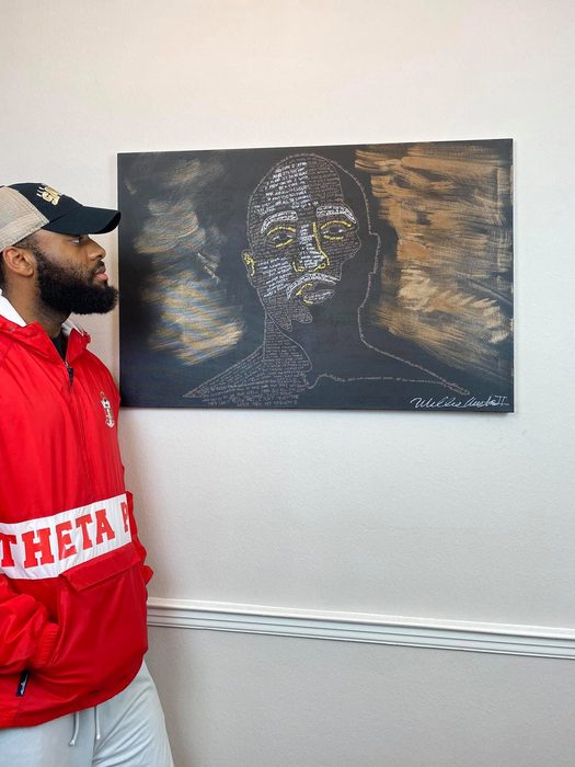 Willie Austin in a red jacket and white cap, leaning beside the word portrait on the wall