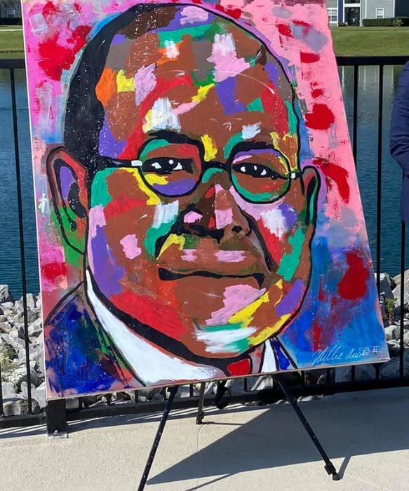 The Dreamer, a colorful portrait of Elder Watson Diggs in round glasses, on an easel outdoors