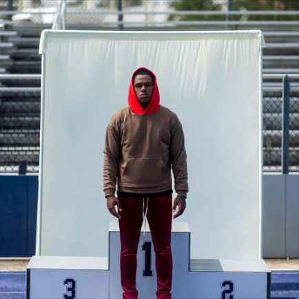 A model on a first place podium in a brown hoodie over a red hood, with red pants