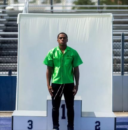 A model on a first place podium in a bright green short sleeve shirt and black pants