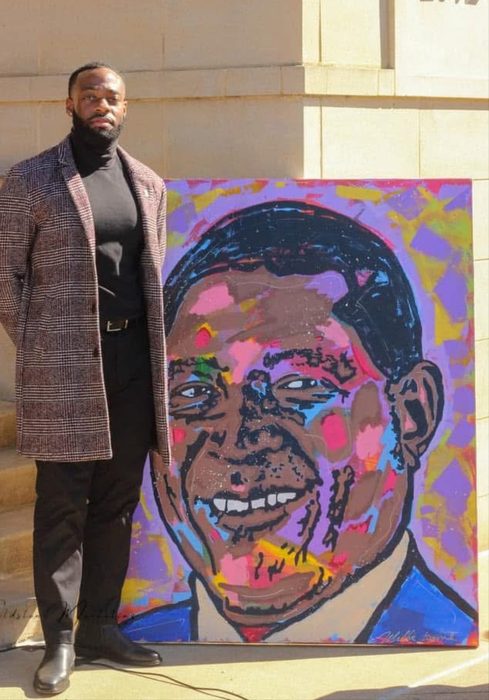 Willie Austin standing outdoors in Selma beside his colorful portrait of Mayor James Perkins Jr.