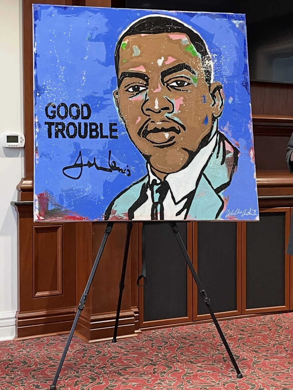 Good Trouble, Willie Austin's portrait of Representative John R. Lewis on a blue background with his signature, on an easel